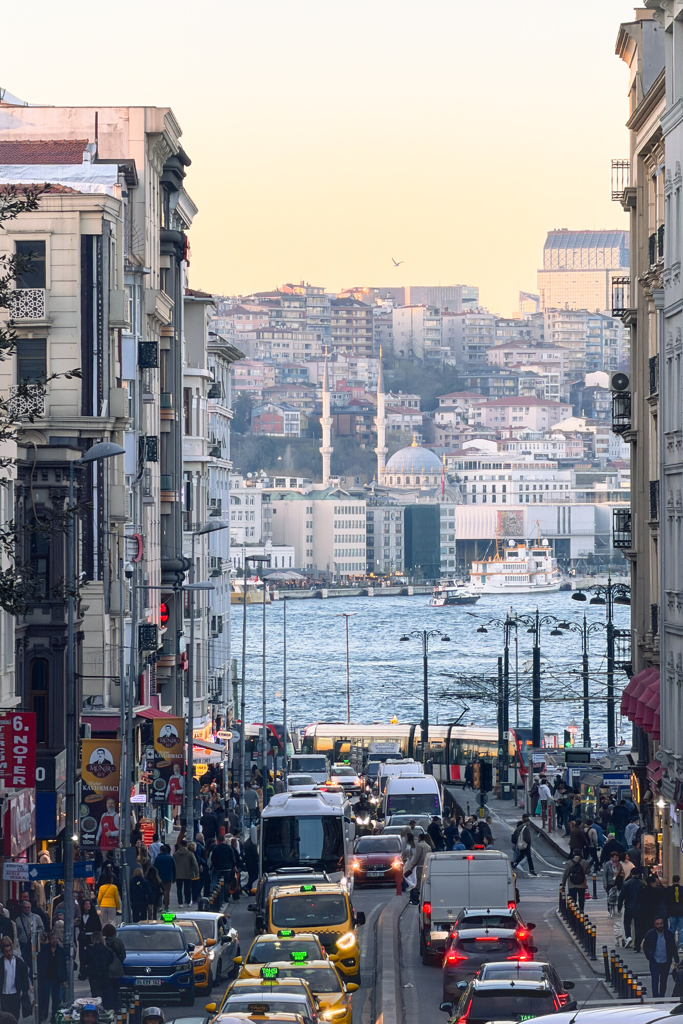 Calle de Estambul con tráfico y peatones, el agua y una mezquita al fondo · iPhone 17 Pro